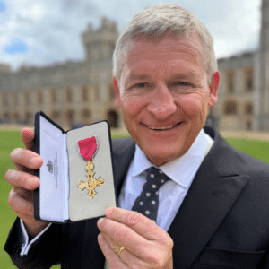 Close-up portrait of Jeremy Kelly holding an open presentation box containing his OBE insignia following his June 2026 investiture at Windsor Castle.